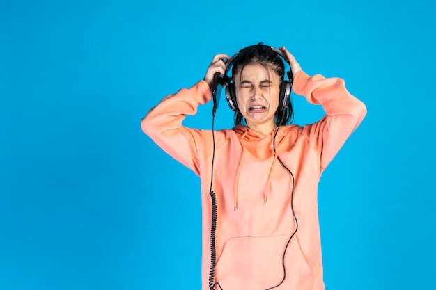 Una niña llorando y quitándose los auriculares con fondo azul.