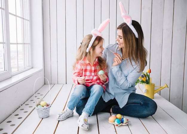 Niña y madre divirtiéndose mientras pintaban huevos para Pascua