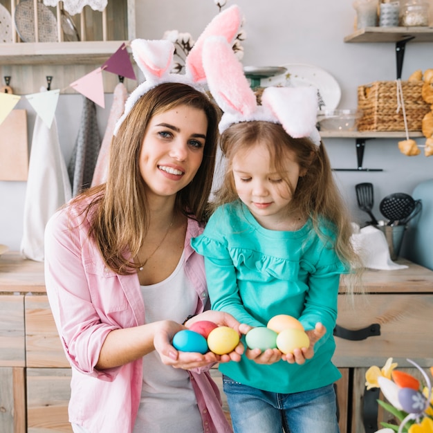 Niña y madre en orejas de conejo con huevos de Pascua en manos