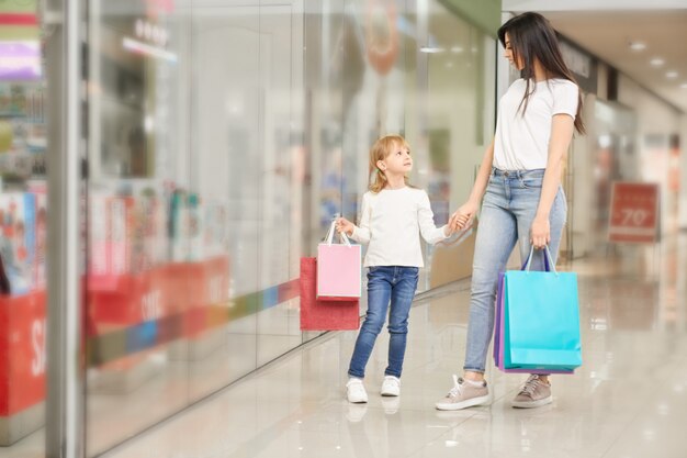 Niña y madre de pie cerca de escaparate del centro comercial.