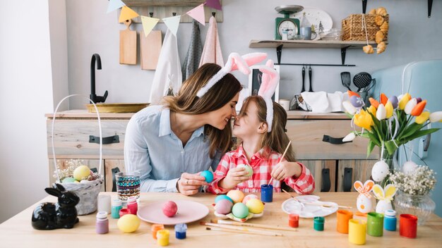 Niña y madre tocando narices mientras pintan huevos para Pascua