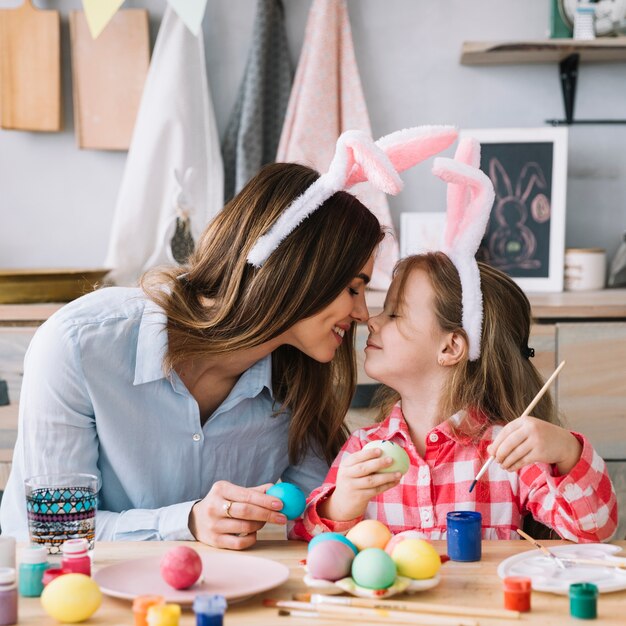 Niña y madre tocando narices mientras pintan huevos para Pascua
