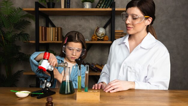 Niña y maestra haciendo experimentos científicos con tubos de ensayo y microscopio