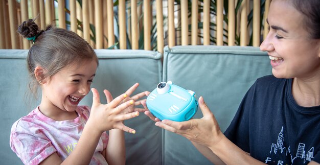 Niña, mamá y una cámara digital de juguete para niños para impresión fotográfica instantánea.