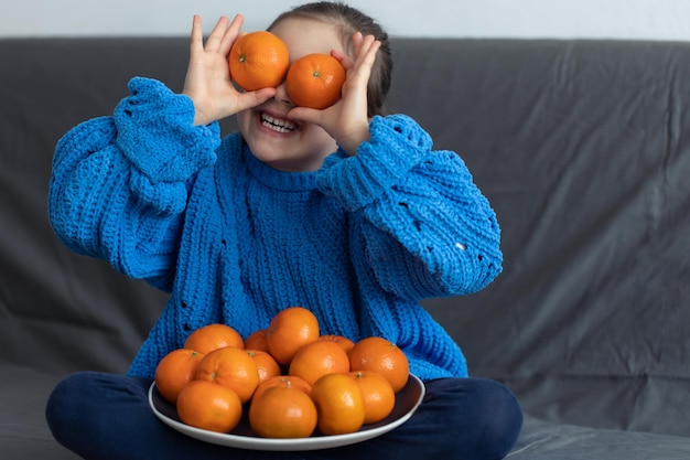 Una niña con mandarinas en casa en el sofá.