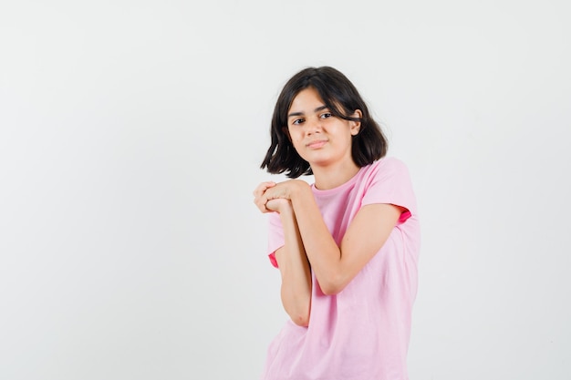 Niña manteniendo las manos juntas en una camiseta rosa y luciendo linda vista frontal.