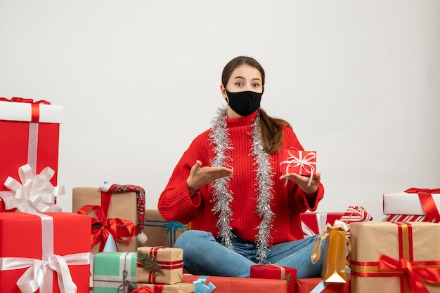 Niña con máscara negra apuntando a su regalo sentado alrededor presenta en blanco