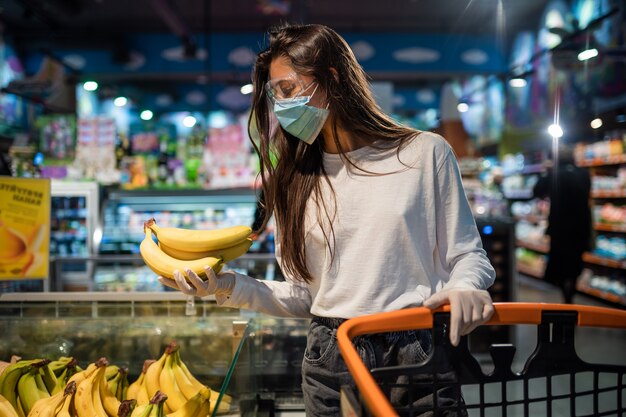 La niña con mascarilla quirúrgica va a comprar plátanos.