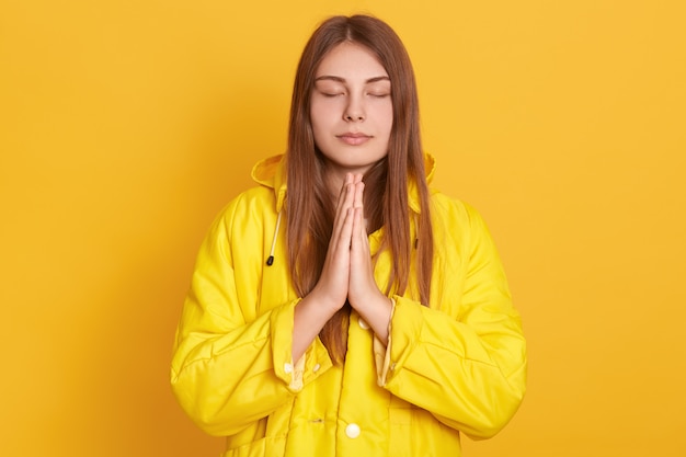 Niña meditando o rezando en la pared amarilla