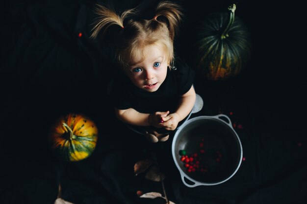 Niña metida en un bol con calabazas alrededor mirando arriba