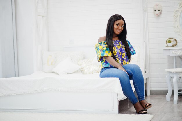 Niña milenaria afroamericana negra en la sala de estar feliz mujer joven de piel oscura el fin de semana en casa sentada en la cama
