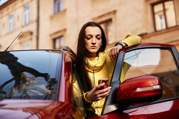 La niña mira el teléfono y se sienta en el coche.