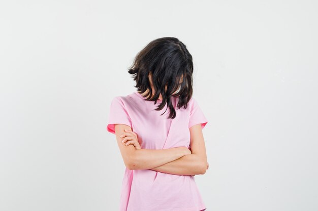 Niña mirando hacia abajo con los brazos cruzados en una camiseta rosa y mirando ofendida. vista frontal.