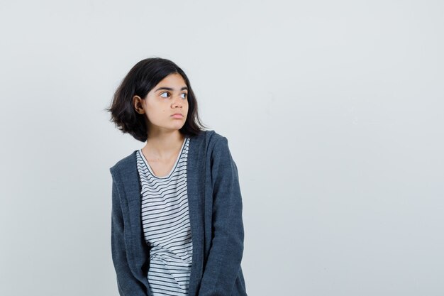 Niña mirando a un lado en camiseta, chaqueta y mirando pensativo.