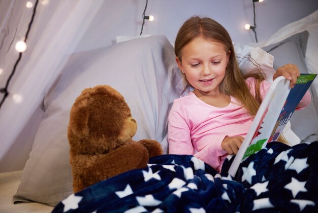 Niña mirando un libro de imágenes con un oso de peluche