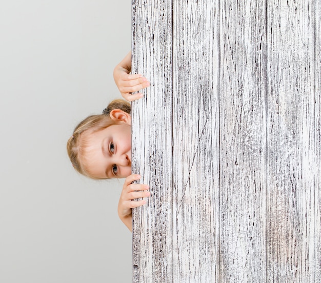 Niña mirando sigilosamente detrás de tablón de madera.