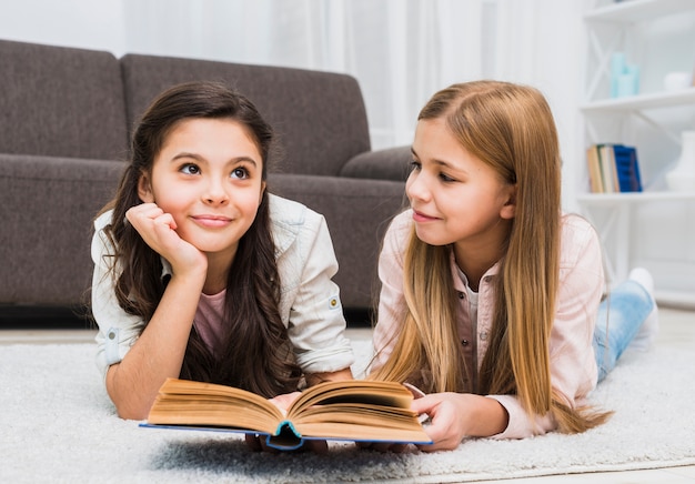 Niña mirando a su amiga pensativa mientras lee un libro en la sala de estar