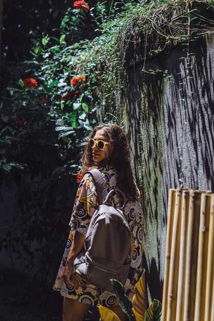 niña con una mochila, con gafas de sol, en un jardín tropical