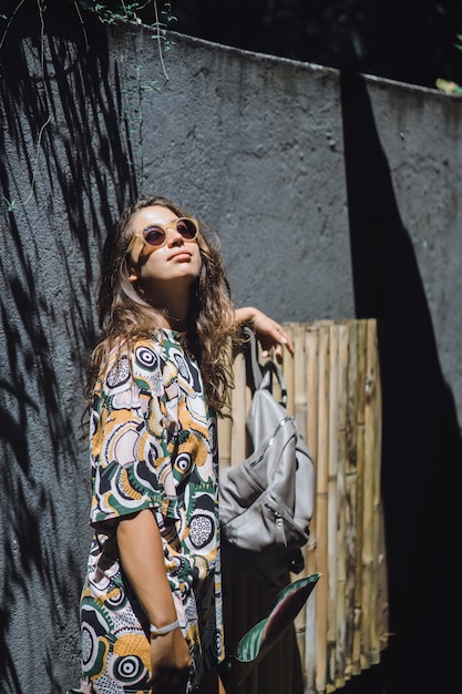 niña con una mochila, con gafas de sol, en un jardín tropical