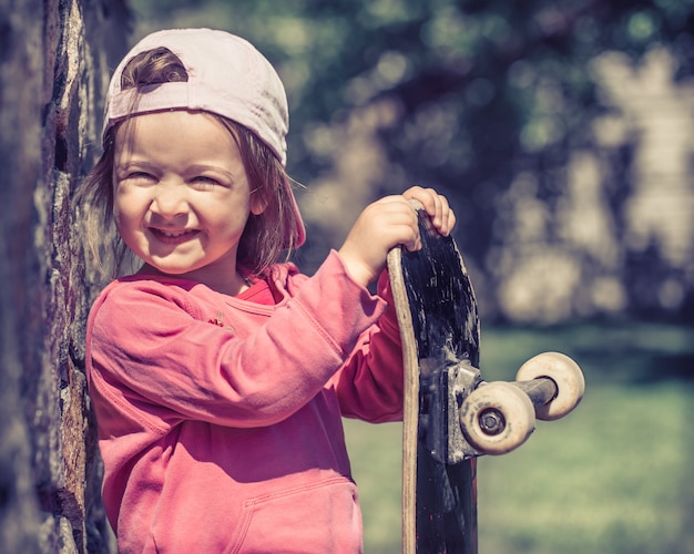 Una niña de moda sostiene una patineta y juega afuera, las hermosas emociones de un niño.