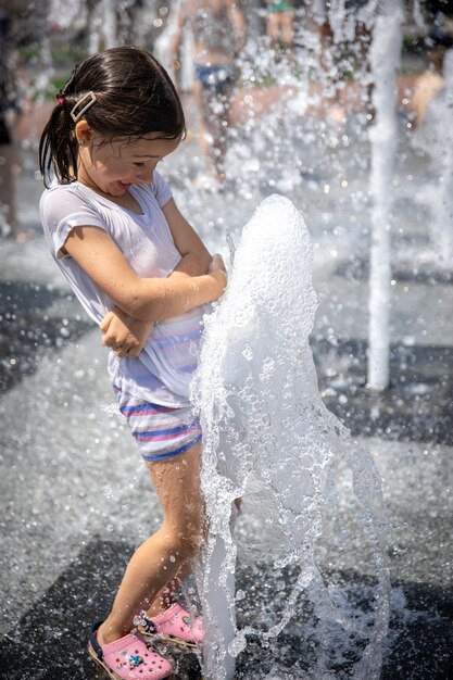 Una niña mojada se está refrescando en una fuente en un caluroso día de verano.