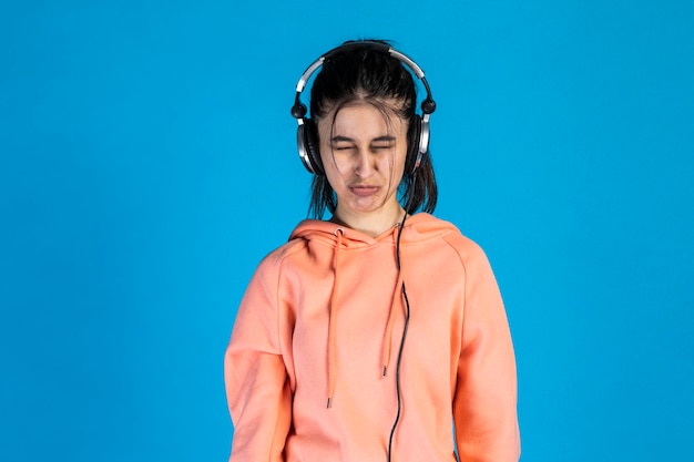 Niña molesta escuchando música y llorando sobre fondo azul Foto de alta calidad