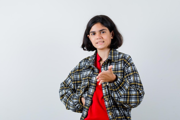 Niña mostrando algo mientras habla en camisa, chaqueta y mirando enfocado, vista frontal.