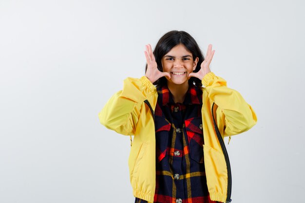 Niña mostrando gesto divertido en camisa a cuadros, chaqueta y luciendo lindo