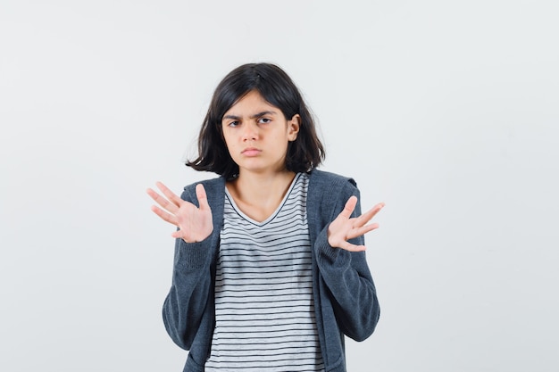 Niña mostrando gesto de impotencia en camiseta, chaqueta y mirando confundido.