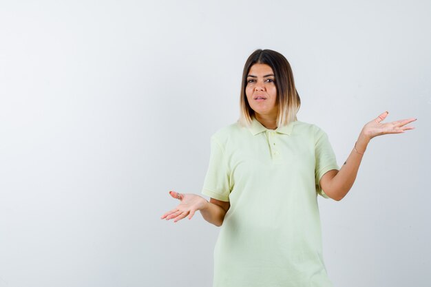 Niña mostrando gesto de impotencia en camiseta y mirando perplejo, vista frontal.