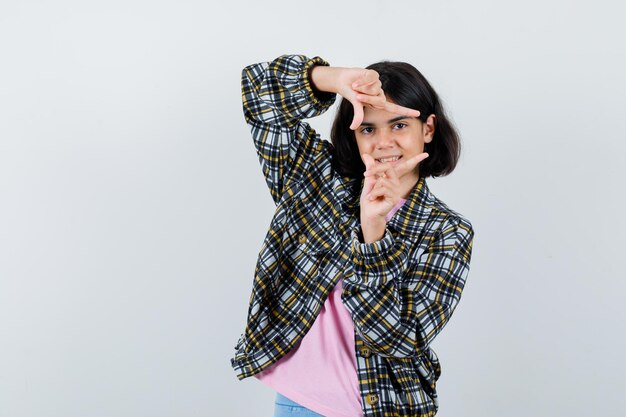 Niña mostrando gesto de marco en camisa a cuadros y camiseta rosa y luciendo lindo. vista frontal.