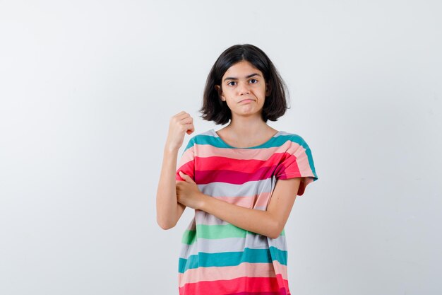 Niña mostrando gesto de poder en camiseta y mirando disgustado. vista frontal.