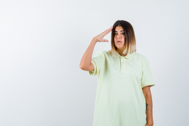 Niña mostrando gesto de saludo en camiseta y mirando serio, vista frontal.