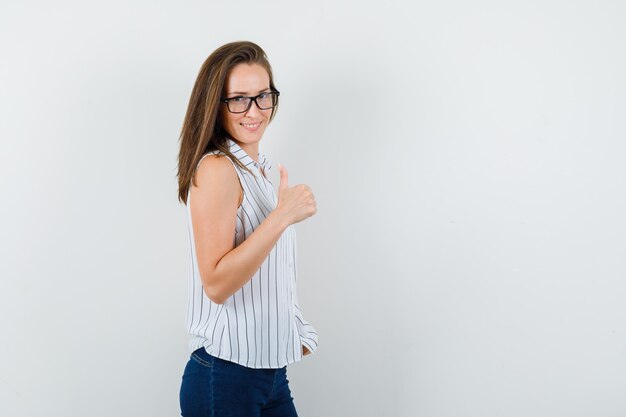 Niña mostrando el pulgar hacia arriba en camiseta, jeans y mirando jovial.