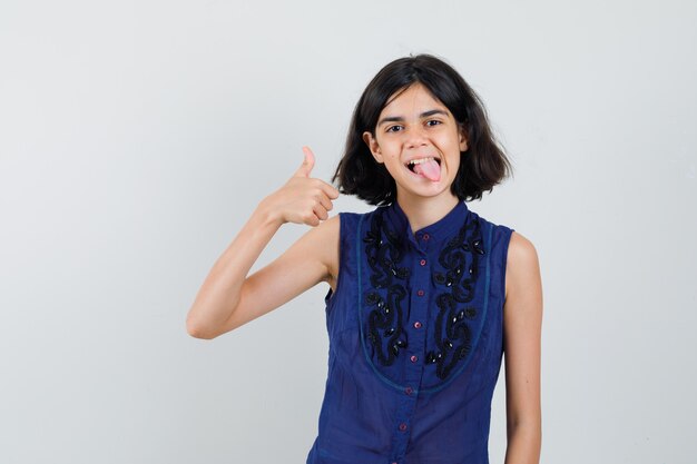 Niña mostrando el pulgar hacia arriba, sacando la lengua en una blusa azul y luciendo feliz.