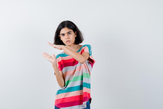 Niña mostrando signo de tamaño pequeño en camiseta y mirando perplejo, vista frontal.