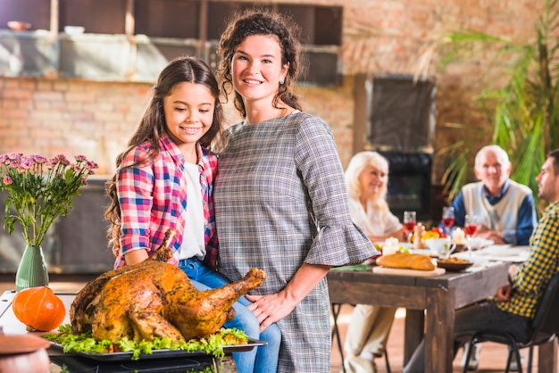 Niña y mujer abrazando cerca de pollo al horno