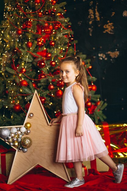 Niña en Navidad en vestido rosa de pie por el árbol de Navidad