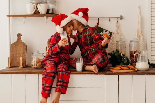 Niña y niño comiendo galletas navideñas y bebiendo leche