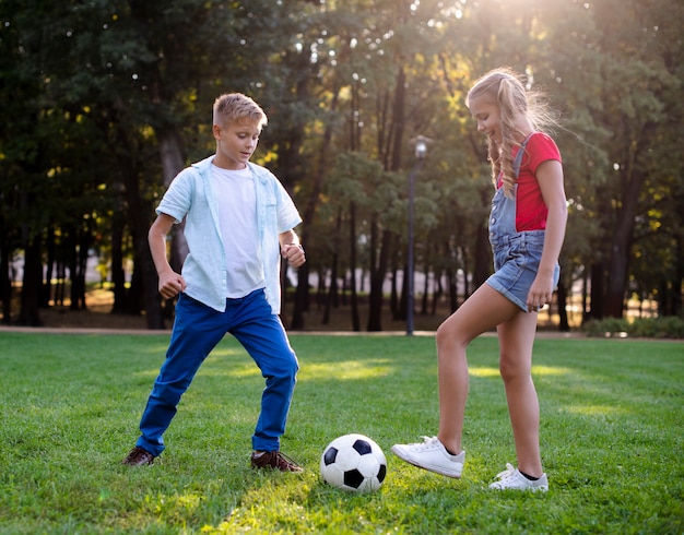 Niña y niño jugando con una pelota en el césped