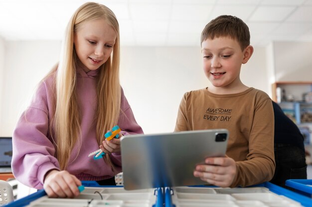 Niña y niño usando una tableta y piezas electrónicas para construir un robot