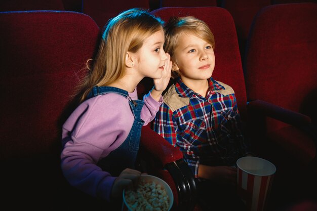 Niña y niño viendo una película en una sala de cine