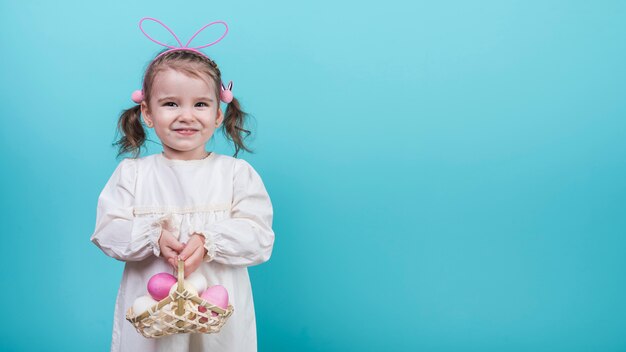 Niña en orejas de conejo con canasta con huevos de Pascua