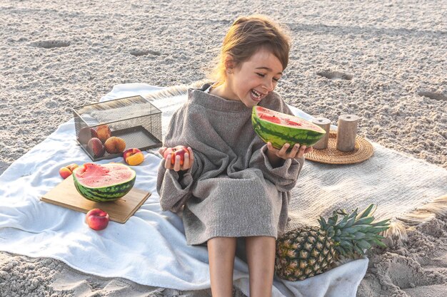 Niña en la orilla del mar de arena en un picnic con frutas