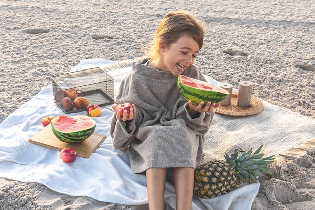 Niña en la orilla del mar de arena en un picnic con frutas