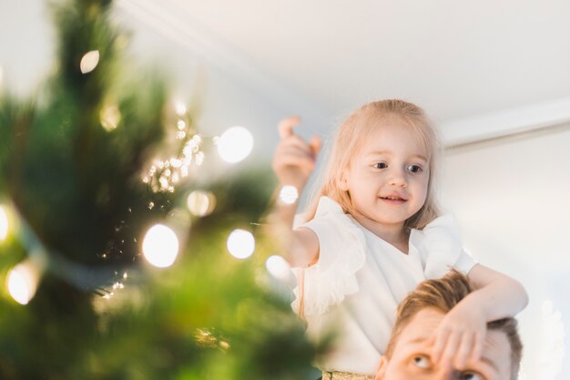 Niña y padre al lado de árbol de navidad iluminado