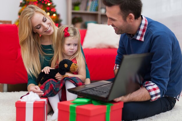 Niña con padres usando laptop en Navidad