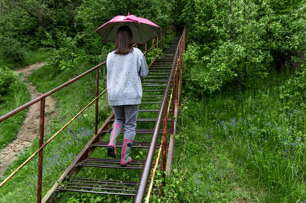 Una niña con un paraguas camina por el bosque en tiempo lluvioso.