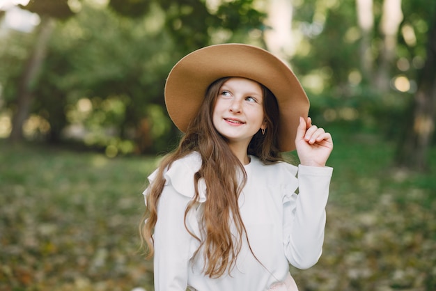 Niña en un parque de pie en un parque con un sombrero marrón