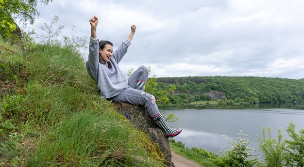 Una niña en un paseo subió una montaña en una zona montañosa y se regocija.